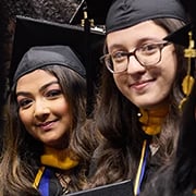 Two female students in cap and gown smiling at SJNY's commencemet ceremony
