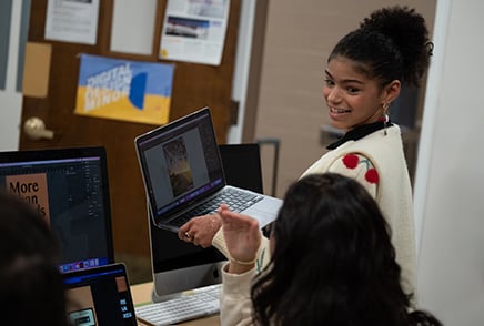 Female student in digital design classroom showing another student her work on her laptop computer