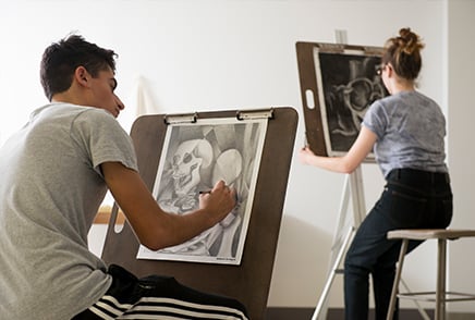 SJNY students at easels creating art on paper with graphite